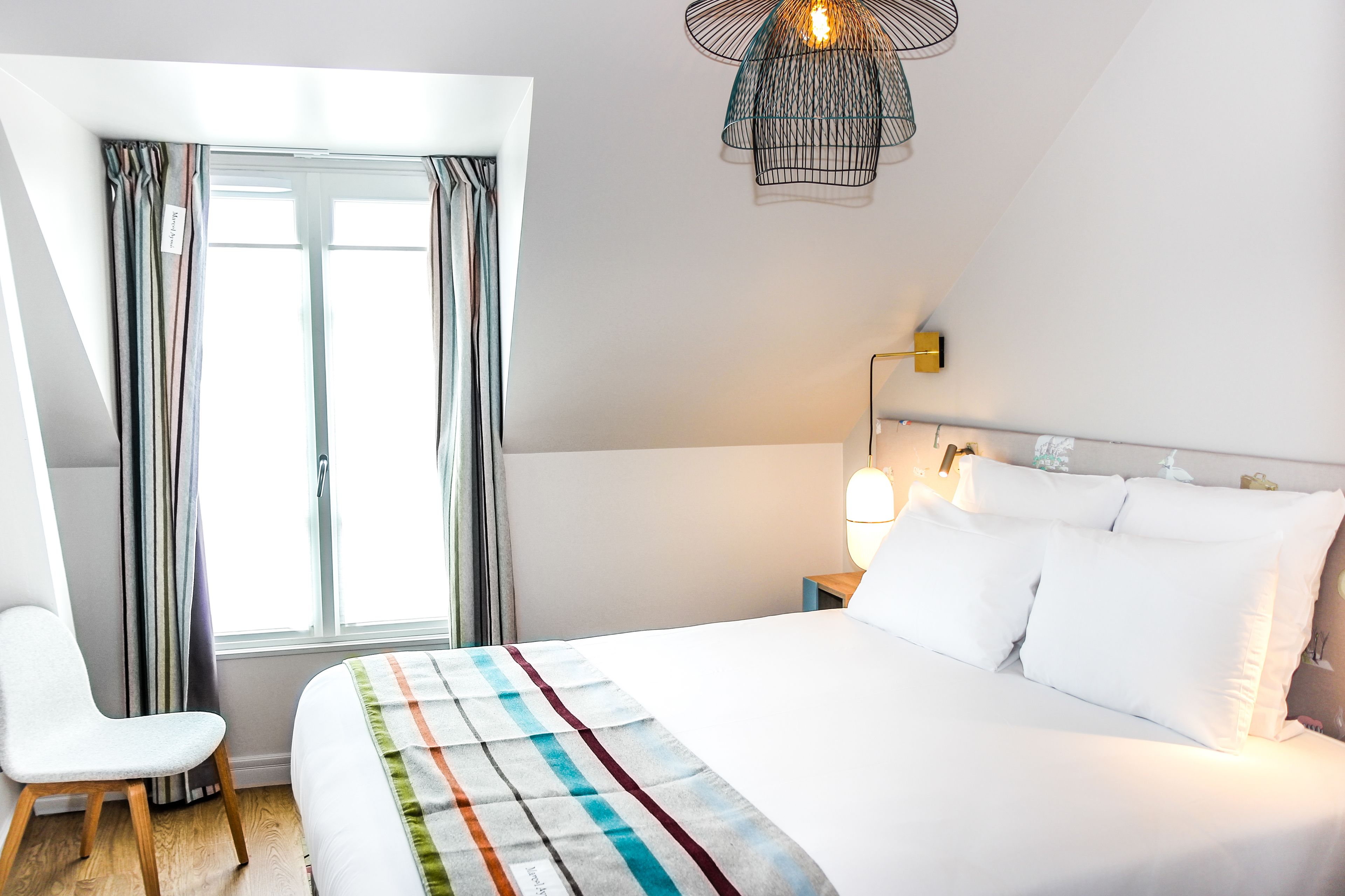 A neatly made bed with white linens, a striped blanket, and a bedside lamp.