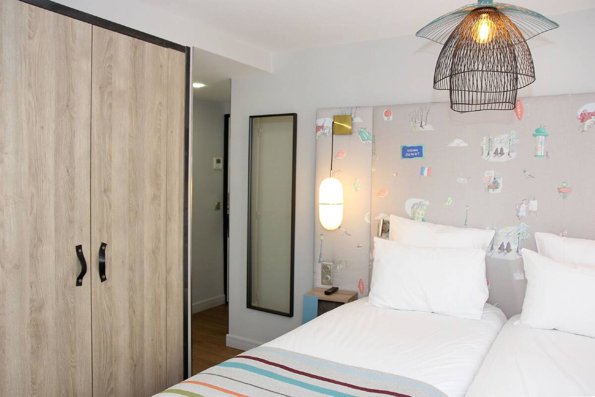 A hotel room with a bed, a wardrobe, a mirror, and a wall with various stickers.