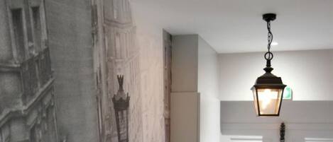 A hallway with a mural of a cityscape, a white door, and a hanging light fixture.