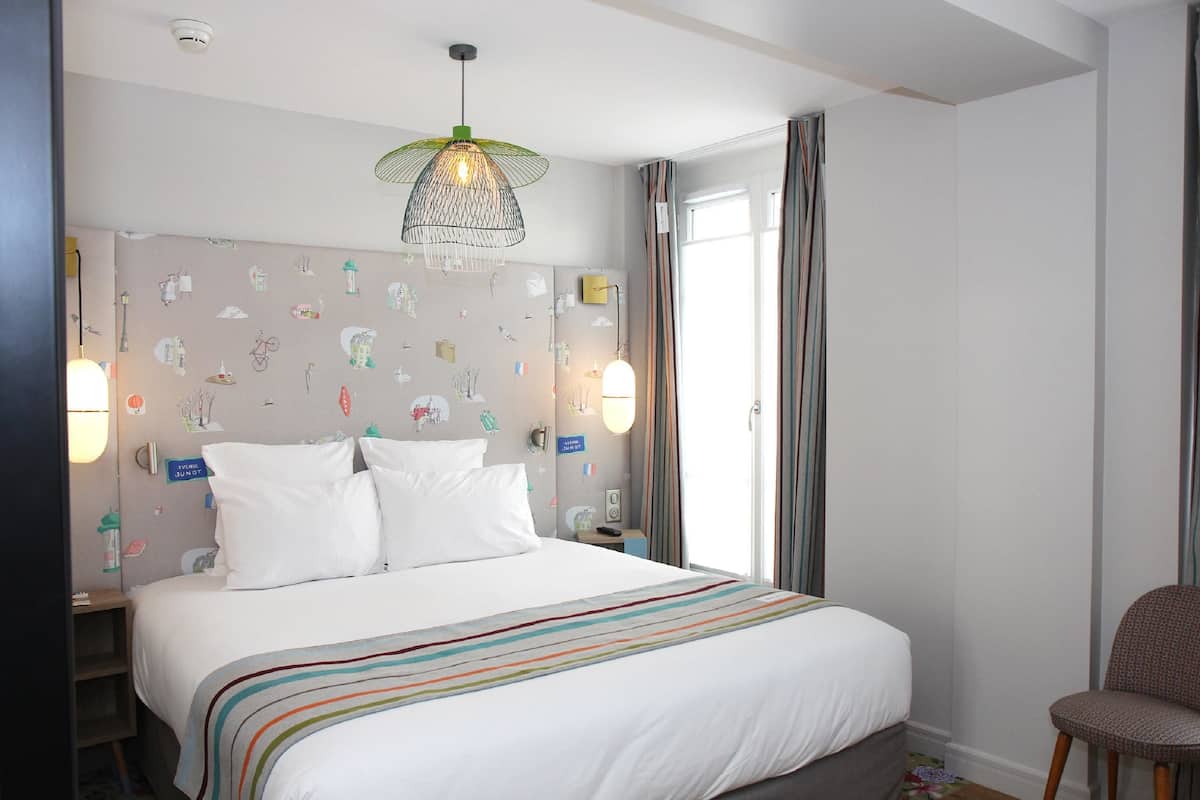 A hotel room with a large bed, a nightstand, a chair, and a window with curtains.