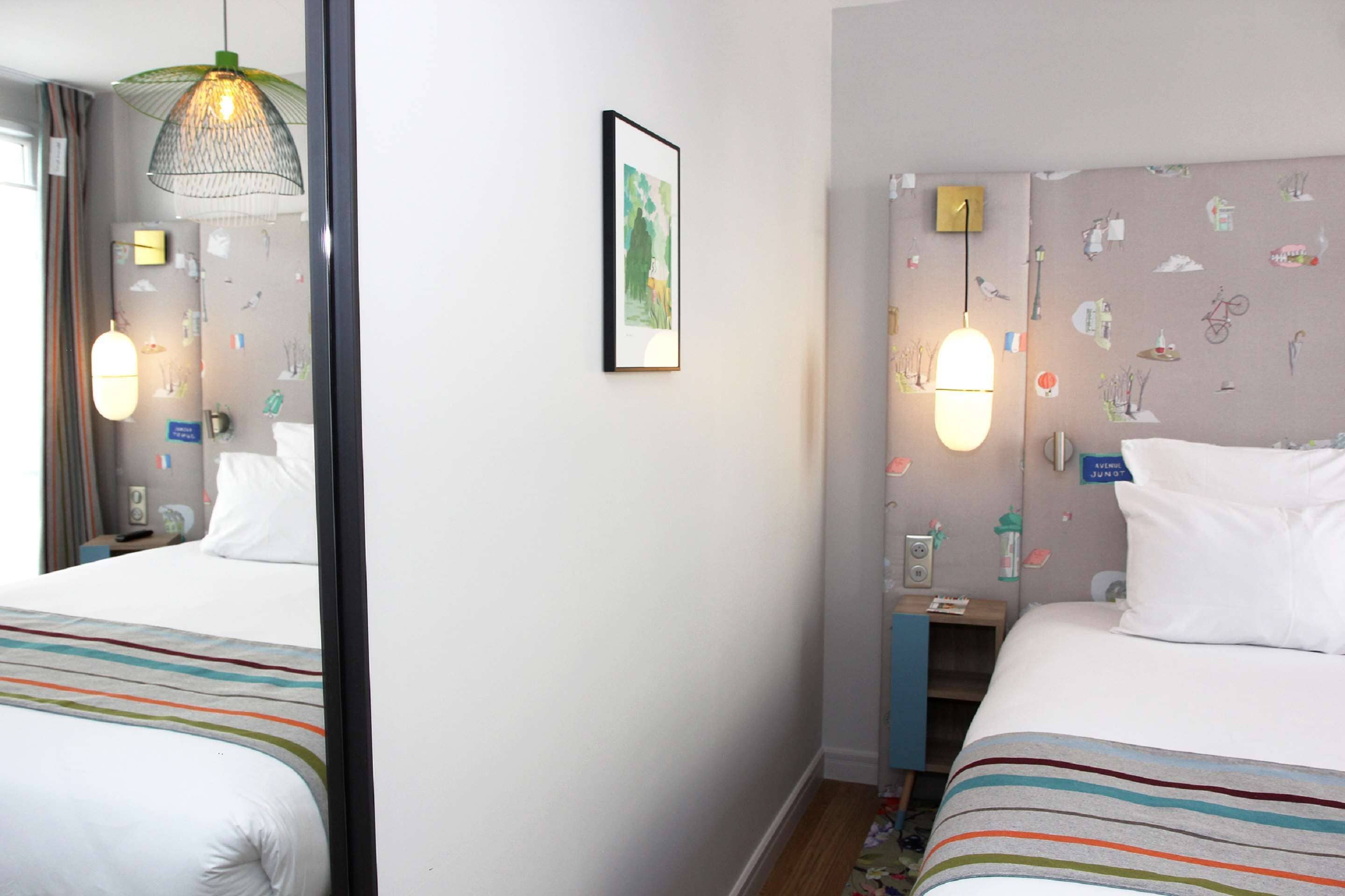 Una habitación de hotel con una cama, una mesita de noche, una lámpara y un espejo.
