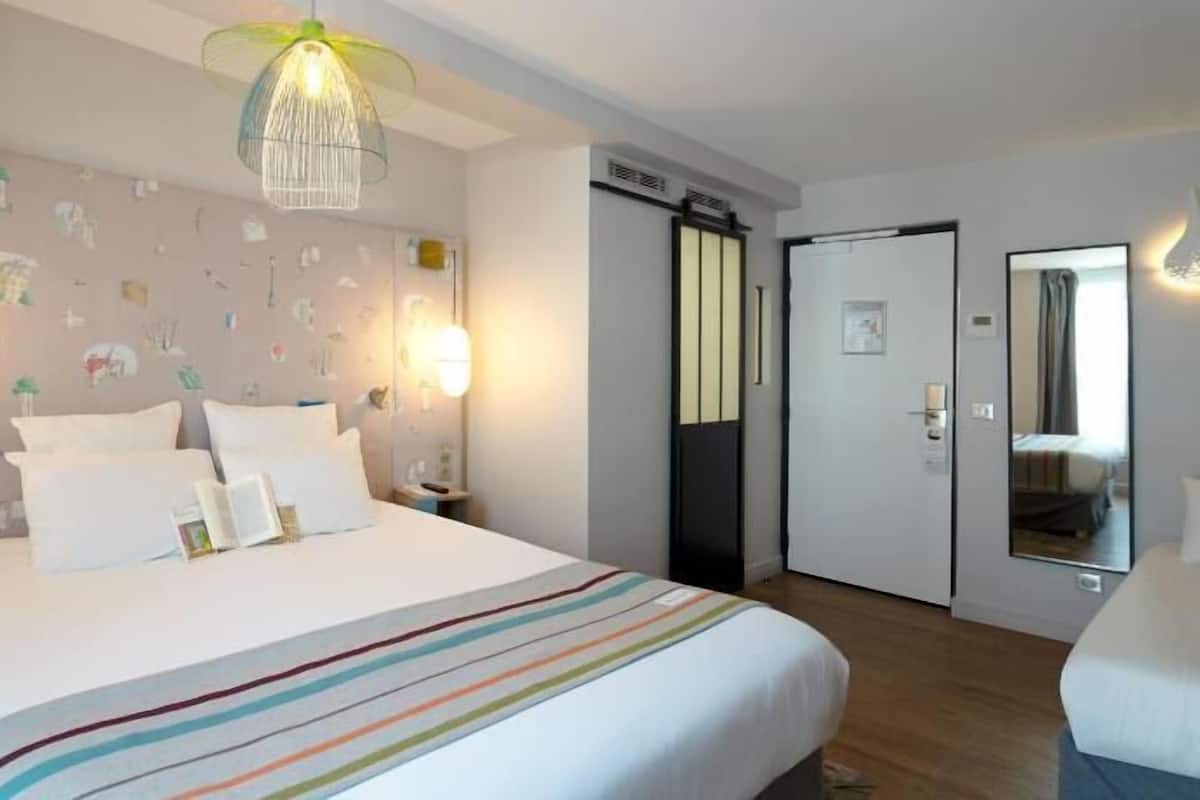 Une chambre d’hôtel comprenant un lit, des tables de chevet, une lampe, un miroir, une armoire et une porte.