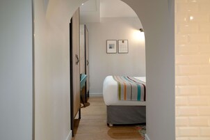 A narrow hallway leading to a bedroom with a bed, a wardrobe, and two framed pictures on the wall.