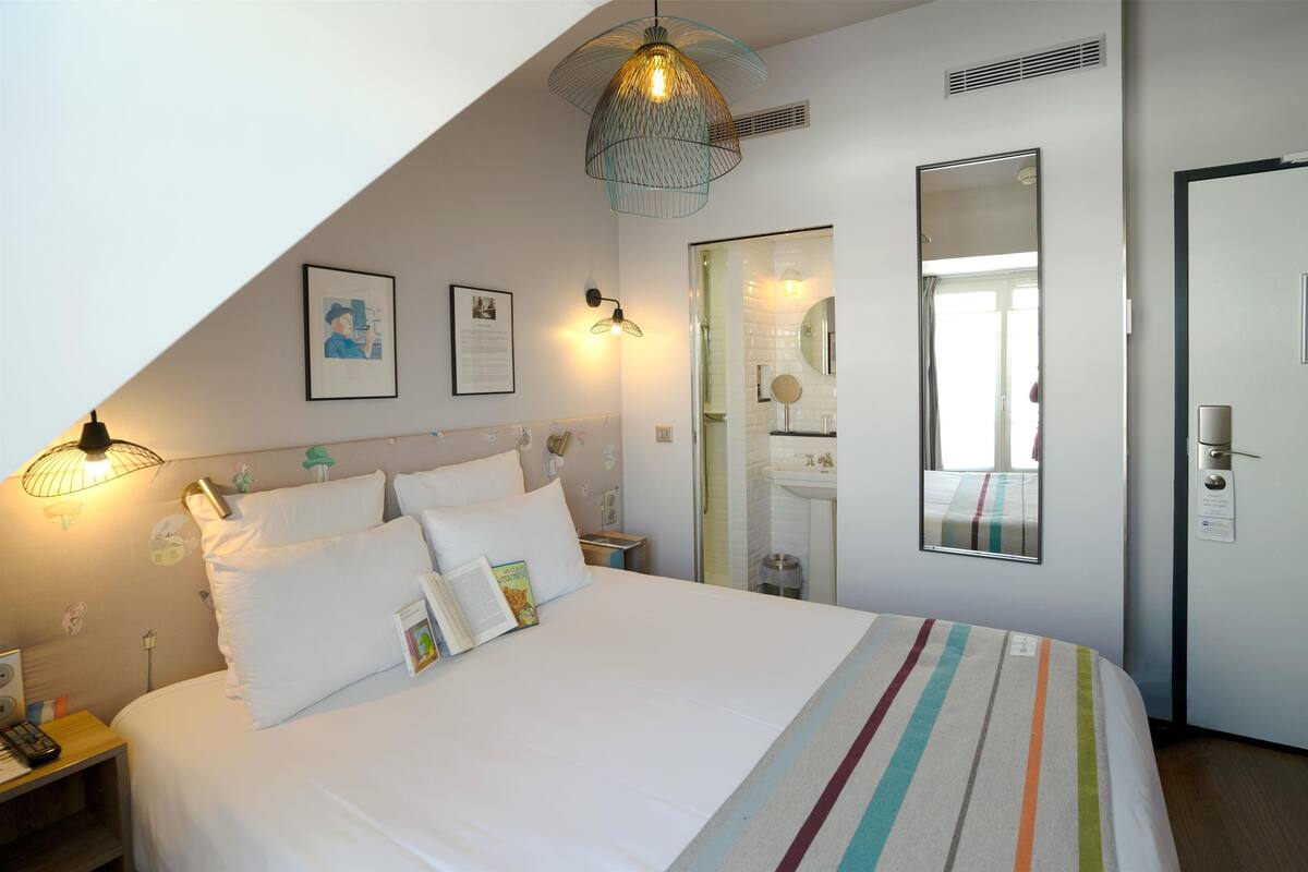 A neatly arranged bedroom with a large bed, bedside lamps, a mirror, and a door.