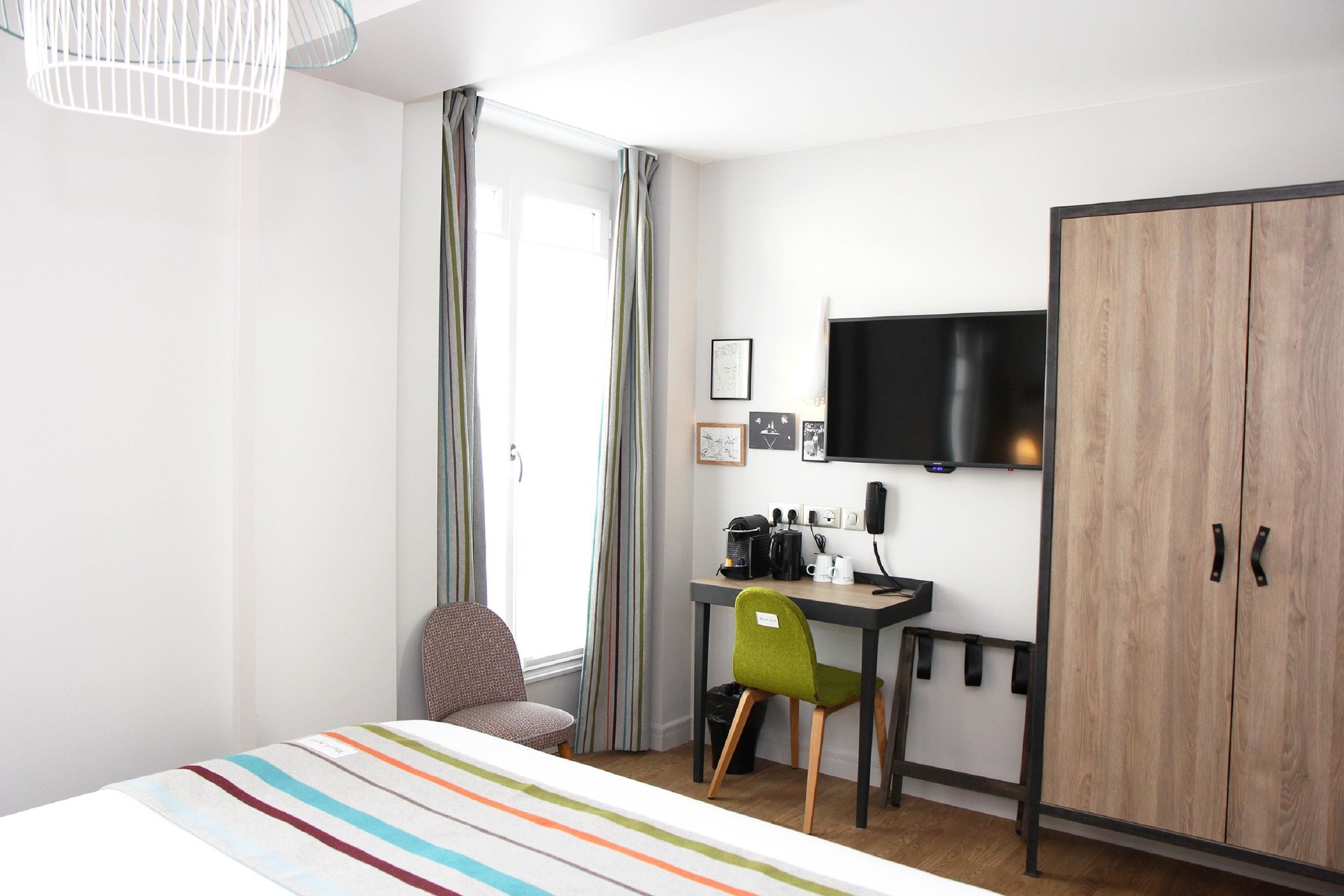 Une chambre d’hôtel de taille réduite, comprenant un lit, un bureau, une chaise, une armoire et un téléviseur.