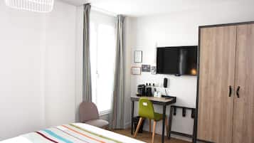 Ein kleines Hotelzimmer mit Bett, Schreibtisch, Stuhl, Kleiderschrank und Fernseher.