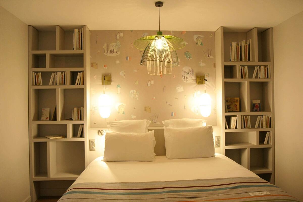 A bedroom with a bed, two bedside tables, a hanging light fixture, and bookshelves on either side.