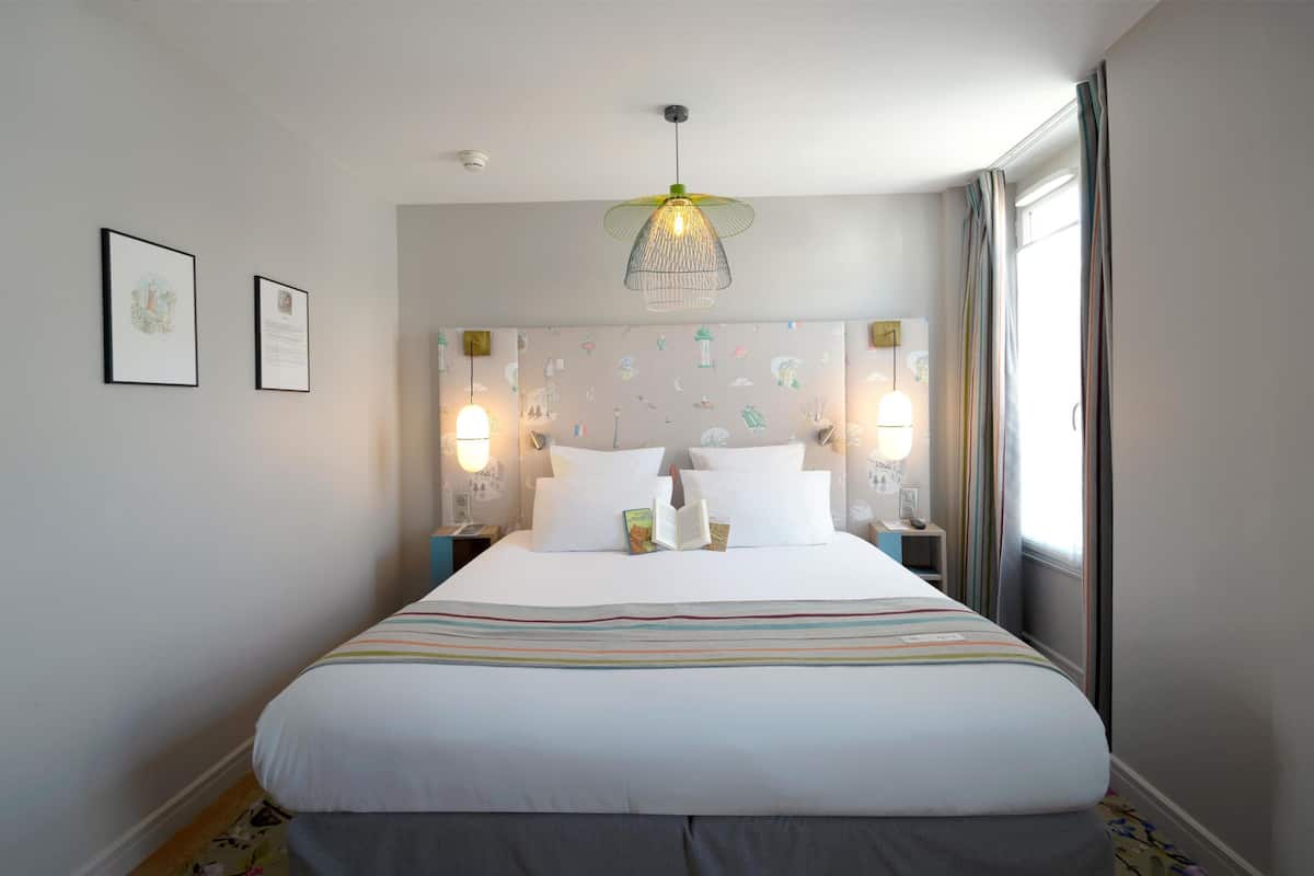 A neatly made bed with white linens, two bedside lamps, and a wall with framed pictures.