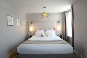 A neatly made bed with white linens, two bedside lamps, and a wall with framed pictures.