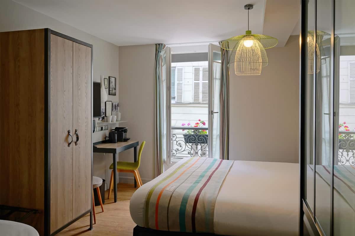 A bedroom with a bed, a desk, a chair, a wardrobe, and a balcony with a railing.