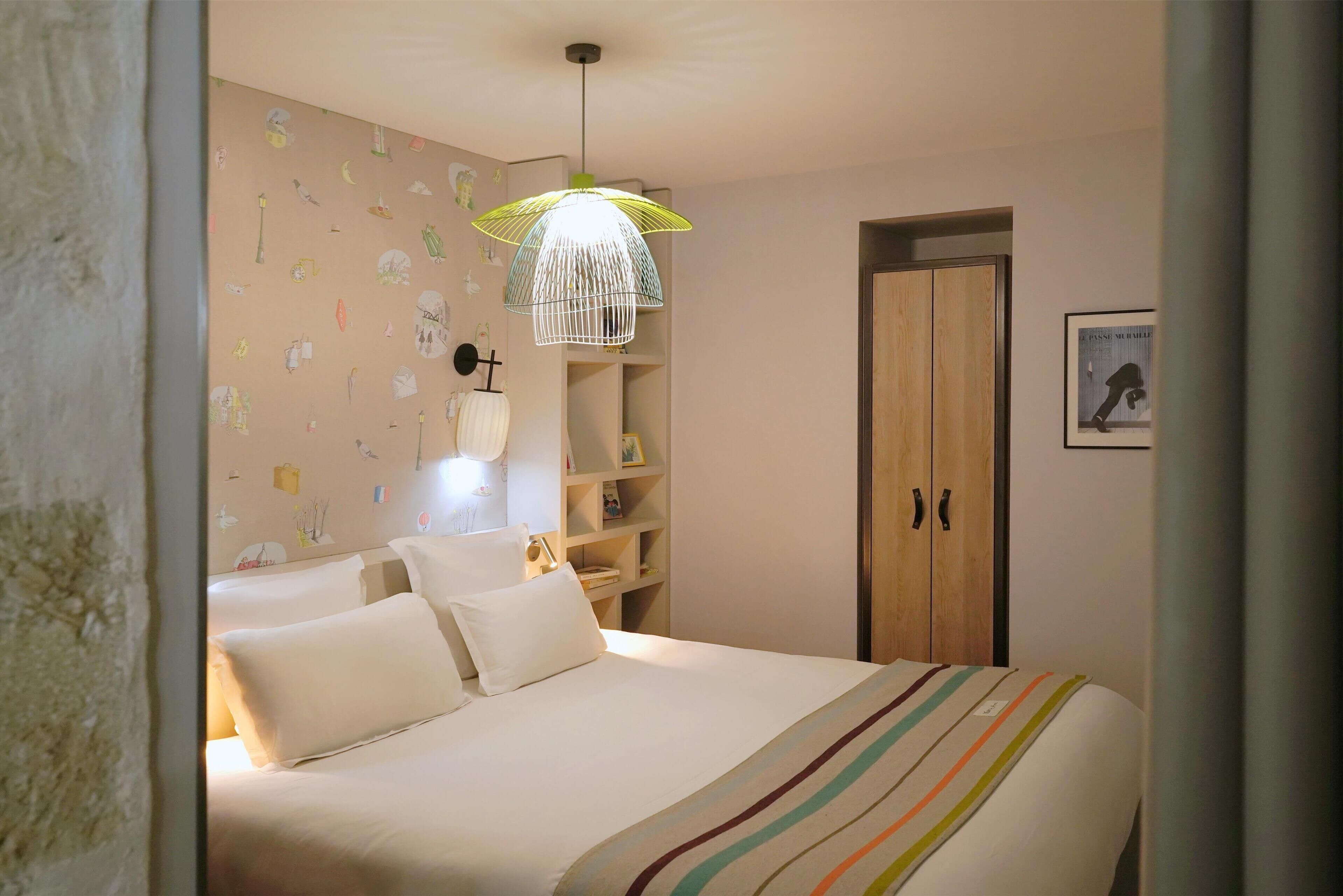 Une chambre à coucher comprenant un lit, une table de chevet, une lampe, une armoire et un luminaire suspendu.