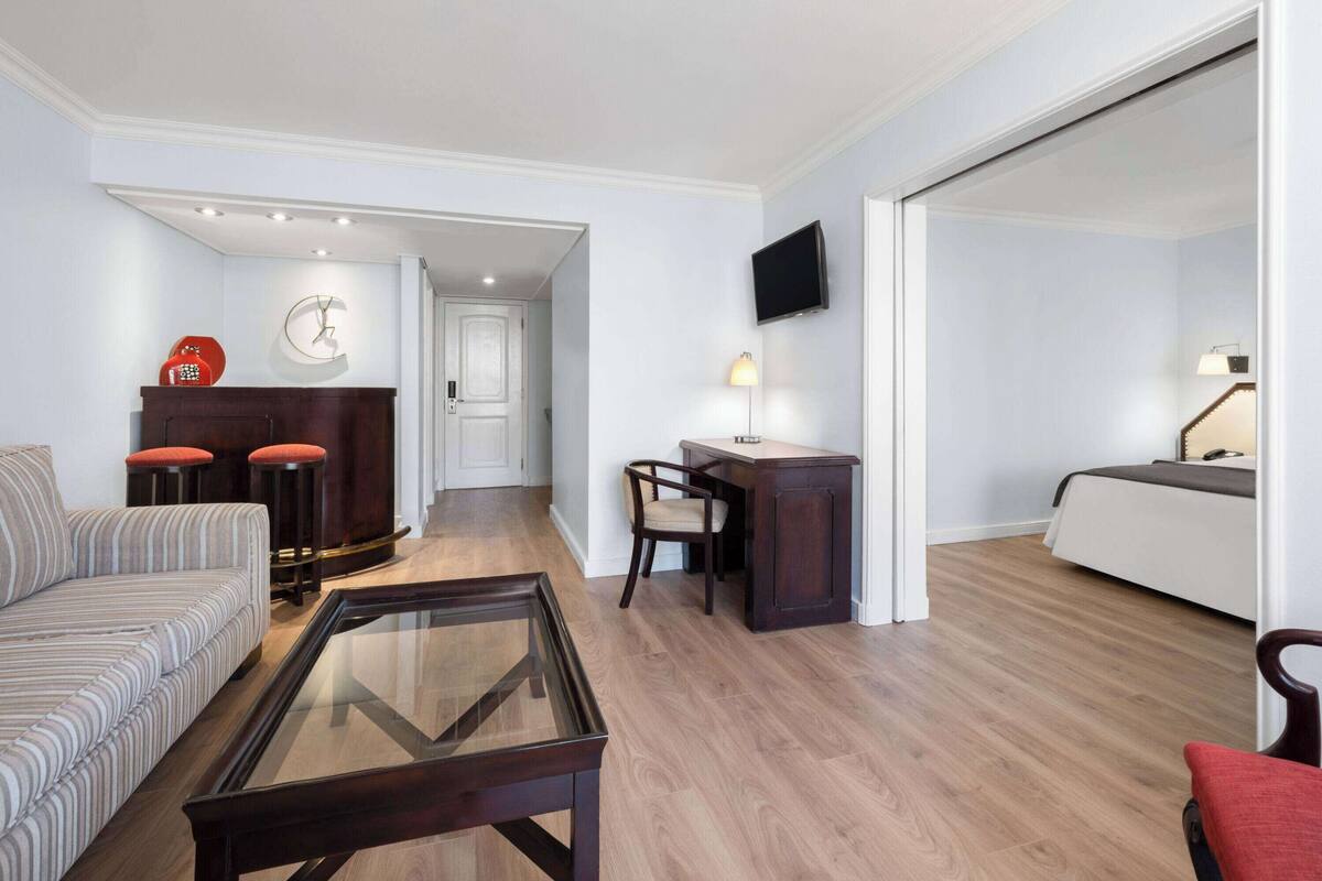 Una sala de estar moderna con un sofá, una mesa de centro de vidrio, un escritorio de madera y un televisor montado en la pared.