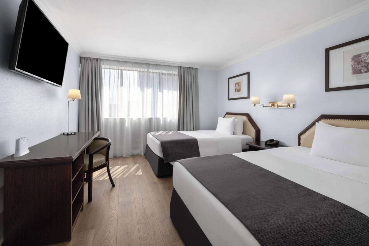 Una habitación de hotel con dos camas, un escritorio, una silla, un televisor y una ventana con cortinas.