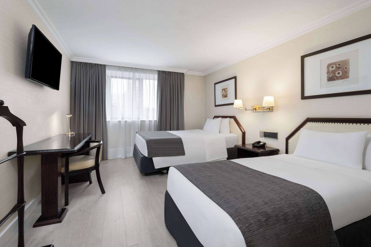 Habitación de hotel con dos camas, un escritorio, una silla, un televisor y una ventana con cortinas.