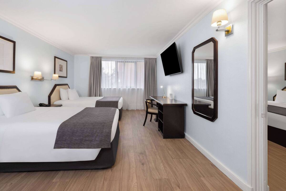 Habitación de hotel con dos camas, un escritorio, una silla, un televisor de pantalla plana y un espejo grande.