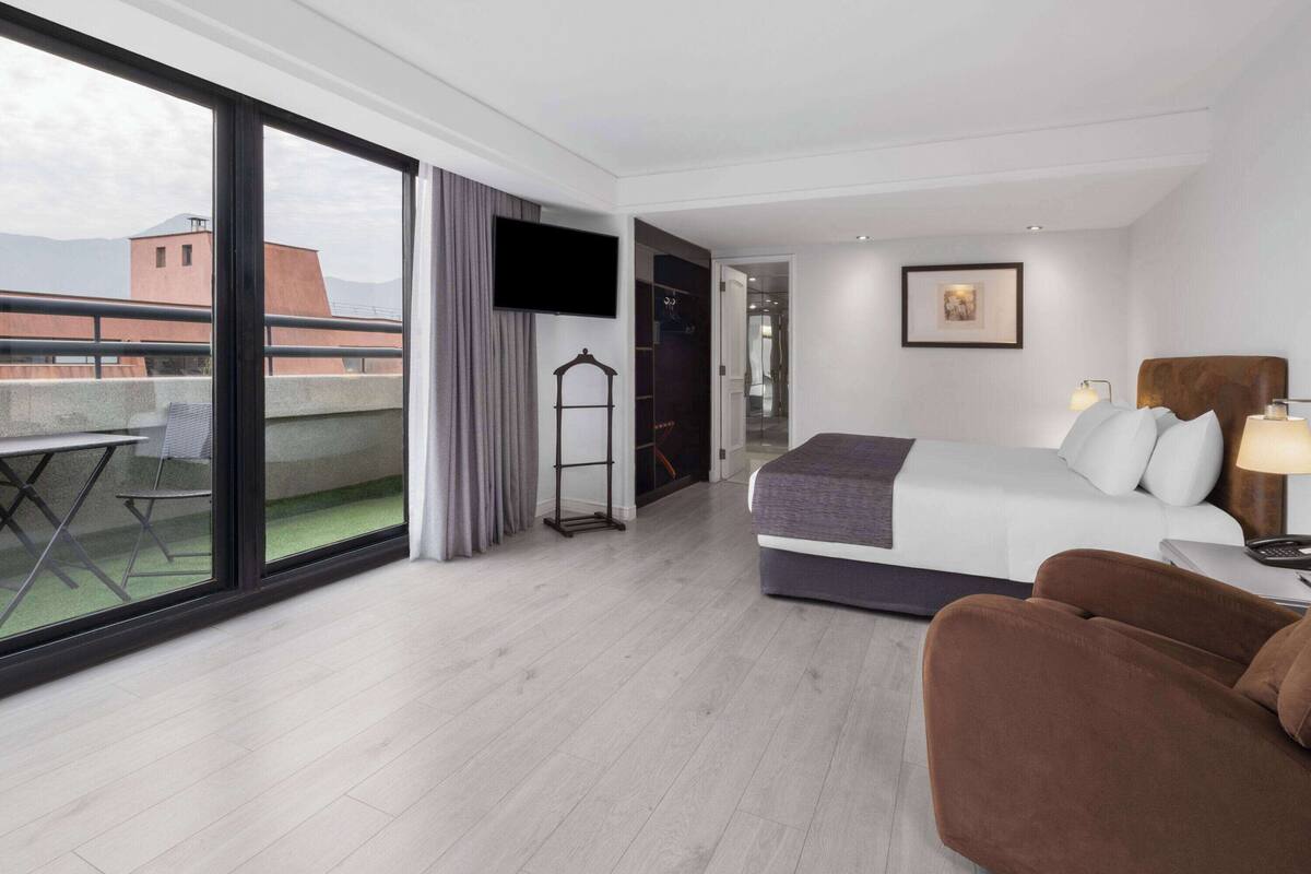 Una habitación de hotel moderna con un balcón amplio, una cama, un escritorio y un televisor.