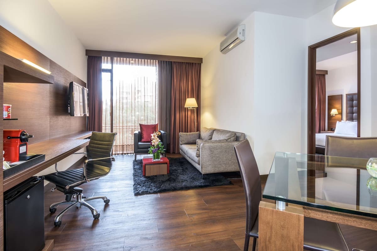 A hotel room with a wooden desk, a sofa, a glass dining table, and a small coffee table.