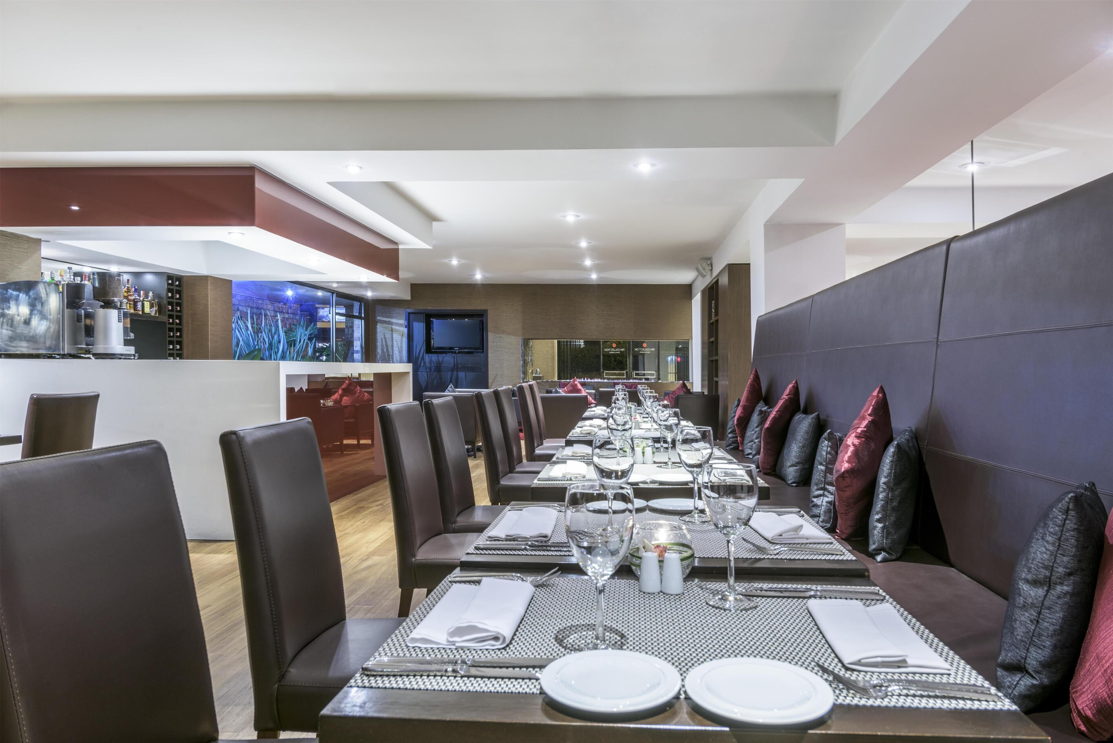 Een restaurant met een lange eettafel gedekt voor een maaltijd, stoelen en een bar in de achtergrond.