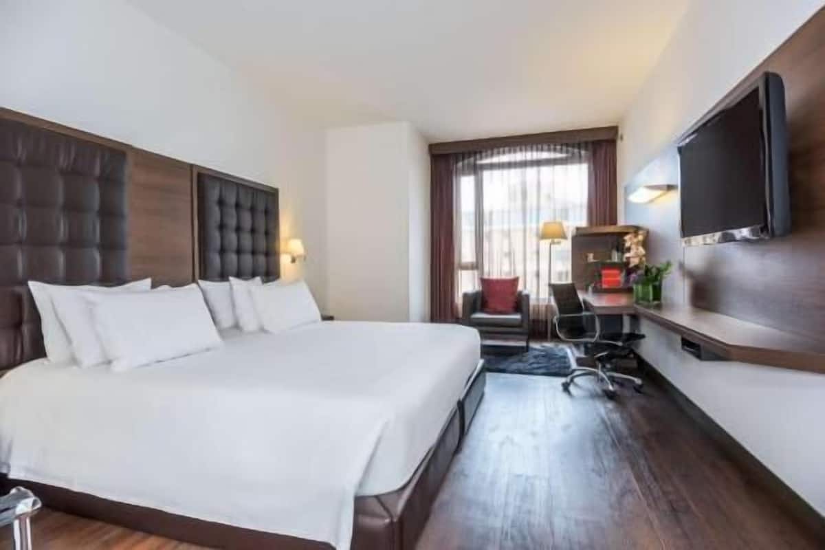 A hotel room with a large bed, a desk, a chair, a TV, and a window with curtains.