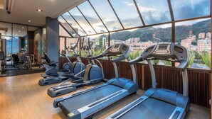 A gym with treadmills, elliptical machines, and a view of a cityscape through large windows. - NH Collection Bogotá Andino Royal (Bogotá)