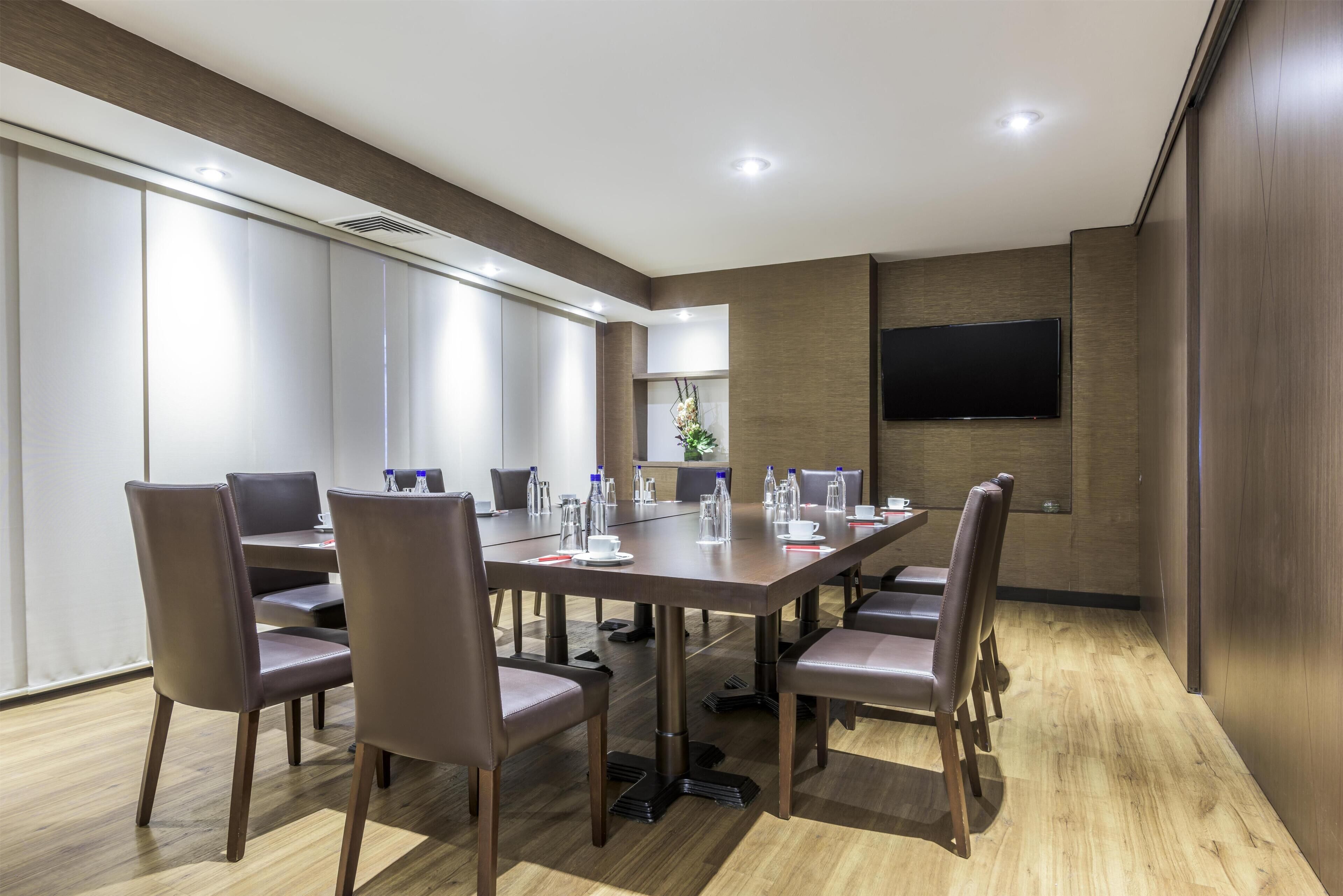 Une salle de conférence avec une longue table, des chaises et un téléviseur à écran plat fixé au mur.
