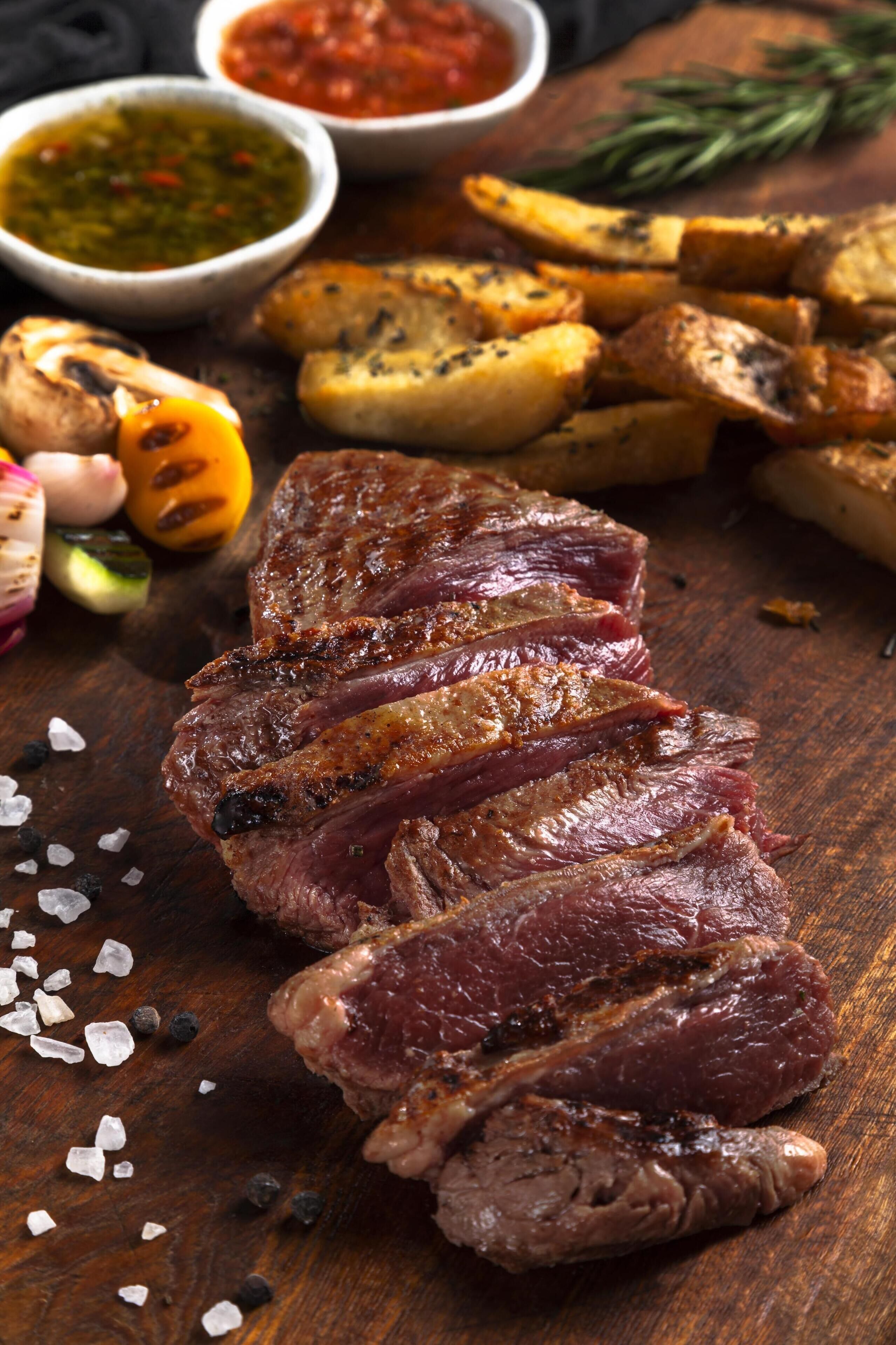 A wooden cutting board with sliced meat, roasted potatoes, and various sauces.