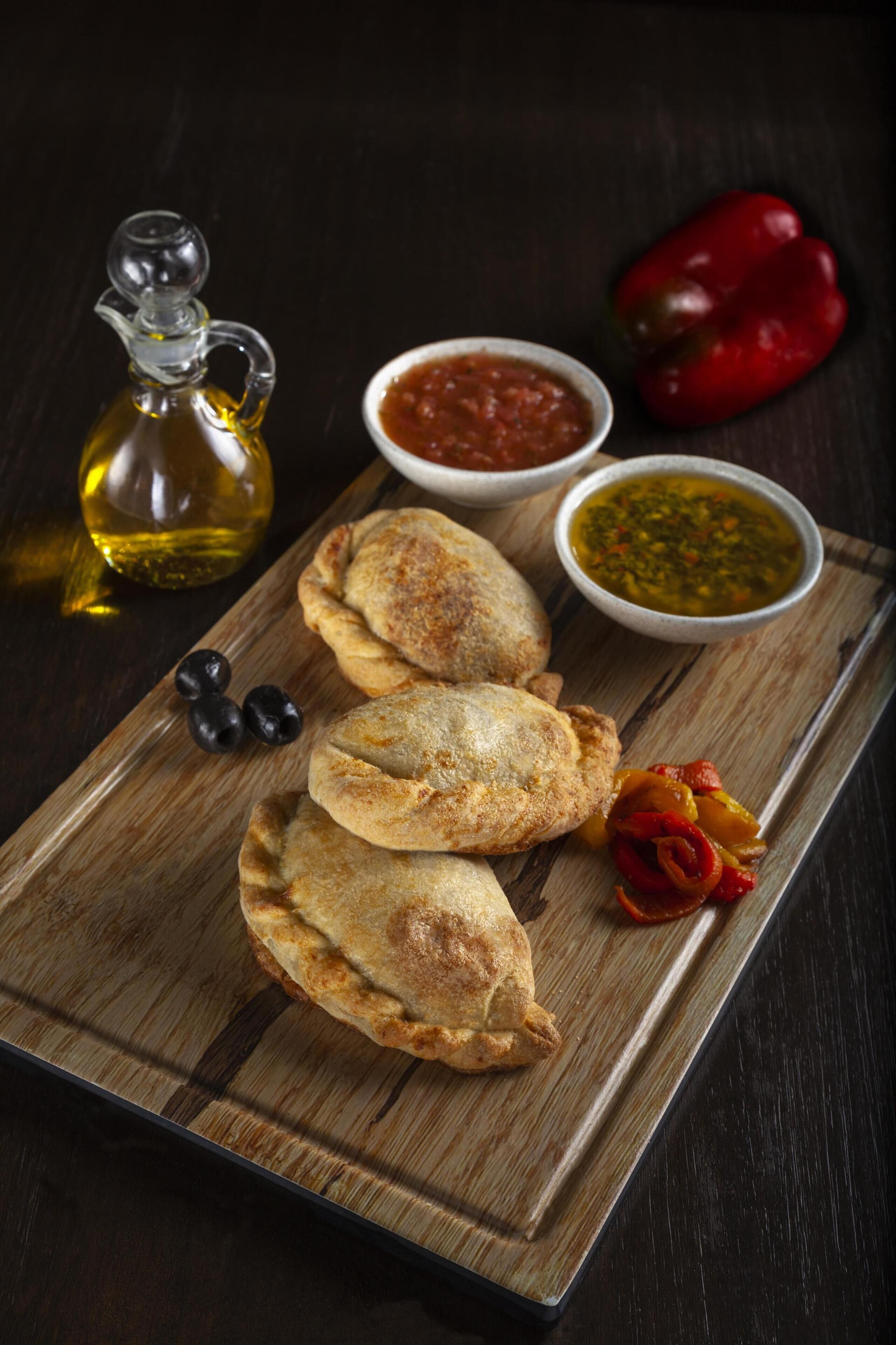 Una tabla de madera con tres pasteles, una botella de aceite y dos recipientes con salsas para mojar.