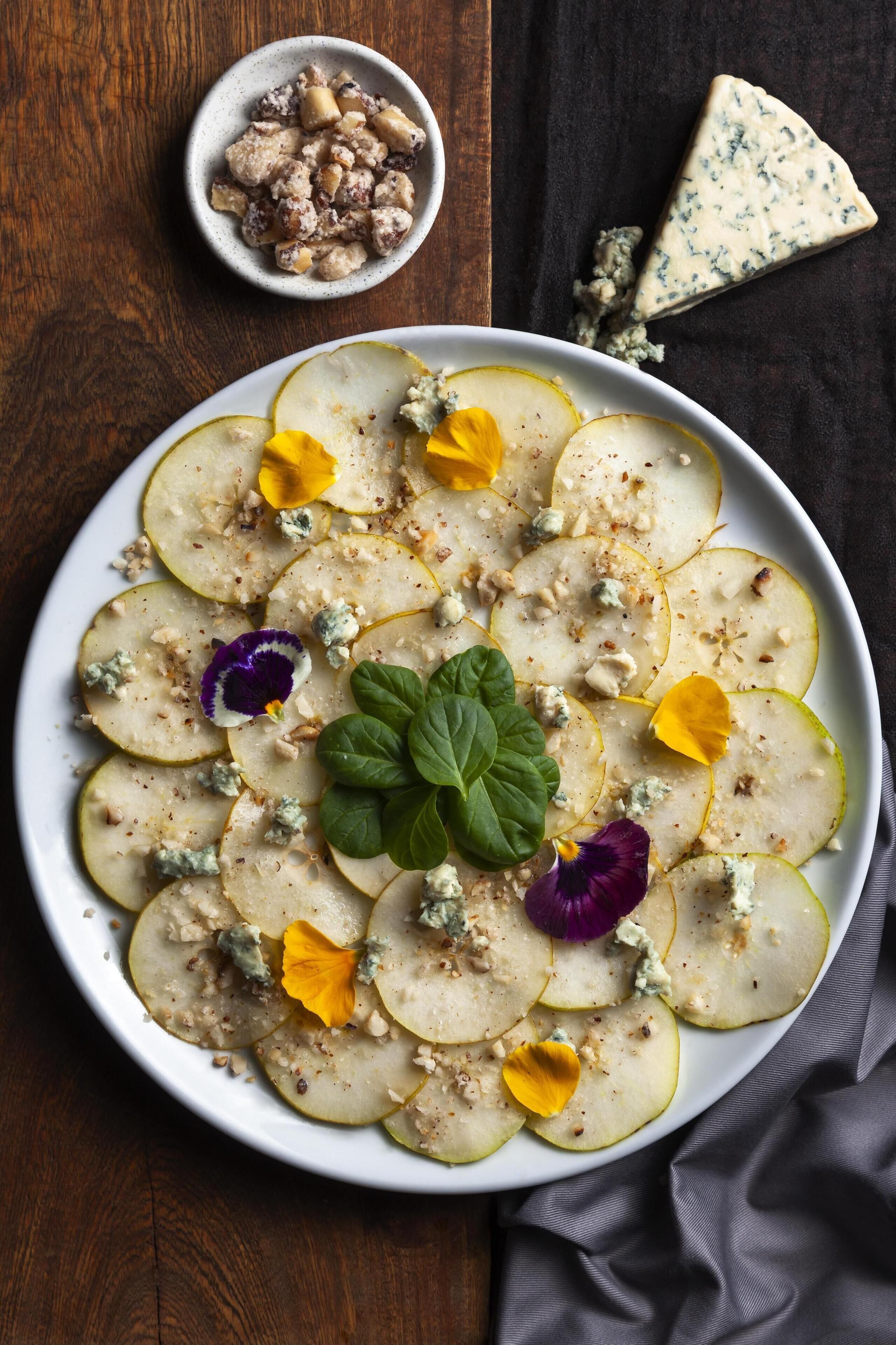 A plate of sliced pears with nuts and blue cheese, garnished with flowers and a mint leaf.