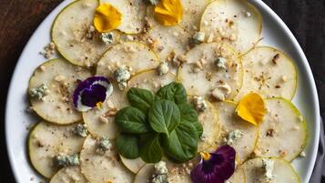 A plate of sliced pears with nuts and blue cheese, garnished with flowers and a mint leaf.