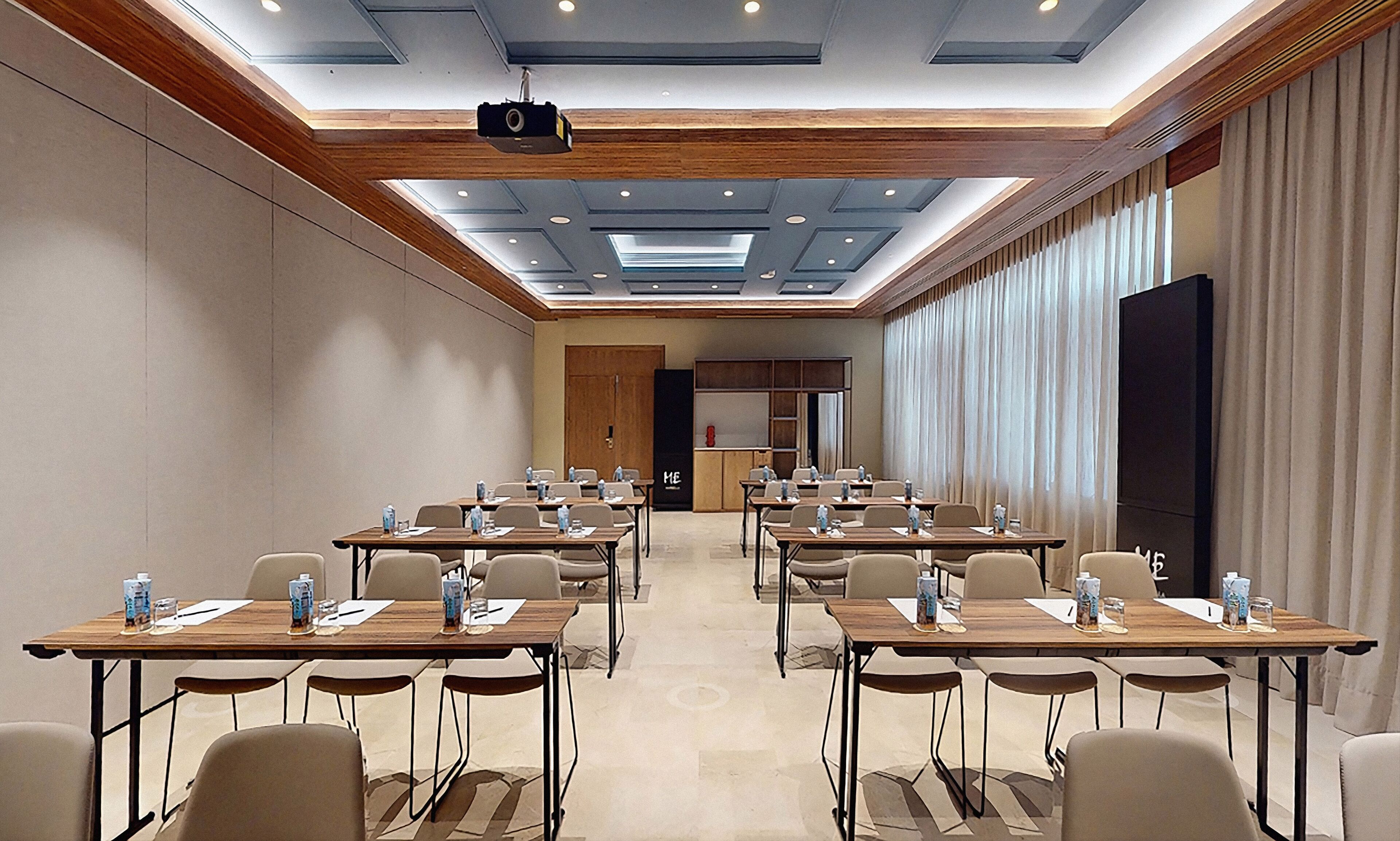 Une salle de conférence équipée de plusieurs tables et chaises, d’un projecteur et d’un grand écran.