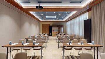 Un salón de conferencias con varias mesas y sillas, un proyector y una pantalla grande.