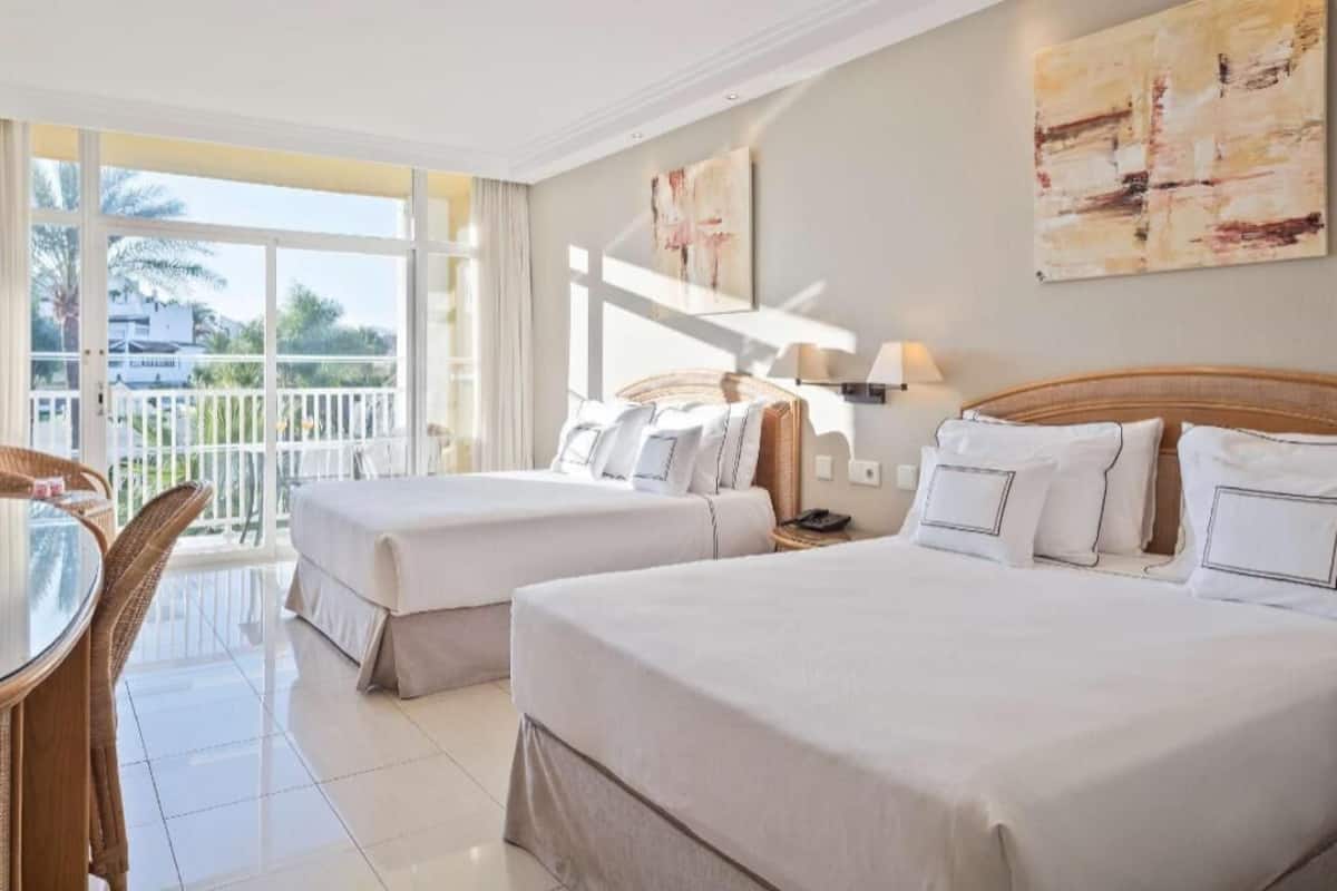 A hotel room with two beds, a balcony, a dining table, and artwork on the walls.