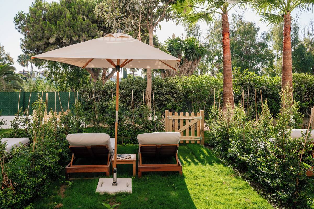 A garden area with two wooden lounge chairs, a table, and a large umbrella.