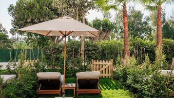 A garden area with two wooden lounge chairs, a table, and a large umbrella.