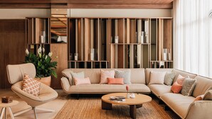 A modern living room with a sofa, armchair, and coffee table. There is a bookshelf with books and decorative items.