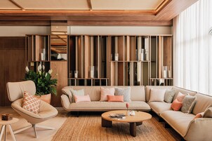 A modern living room with a sofa, armchair, and coffee table. There is a bookshelf with books and decorative items.