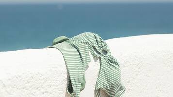 Dos toallas verde y blanco a rayas sobre una superficie blanca, con un cielo azul despejado y el océano al fondo.