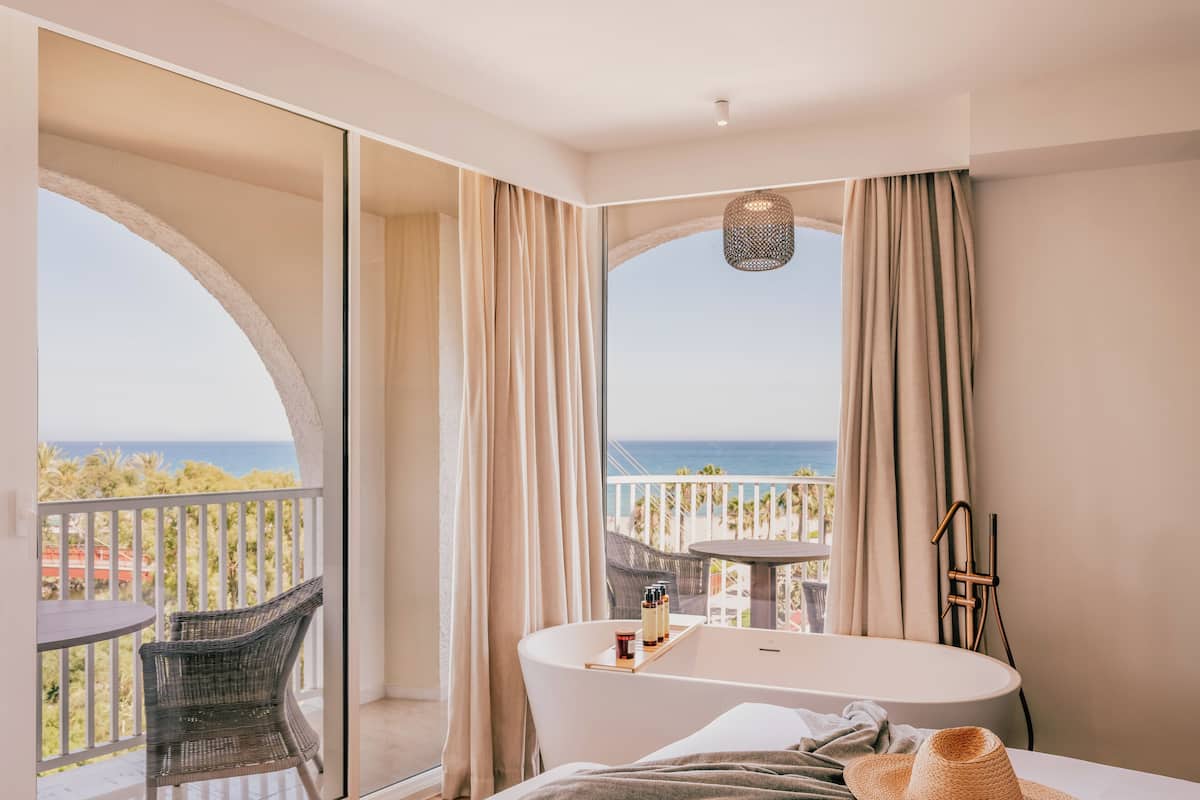 A hotel room with a balcony, a bathtub, and a view of the sea.