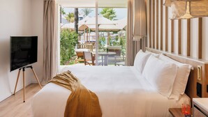 Une chambre d’hôtel avec un grand lit, un téléviseur posé sur un meuble et une vue sur l’espace extérieur, avec des parasols et des palmiers.