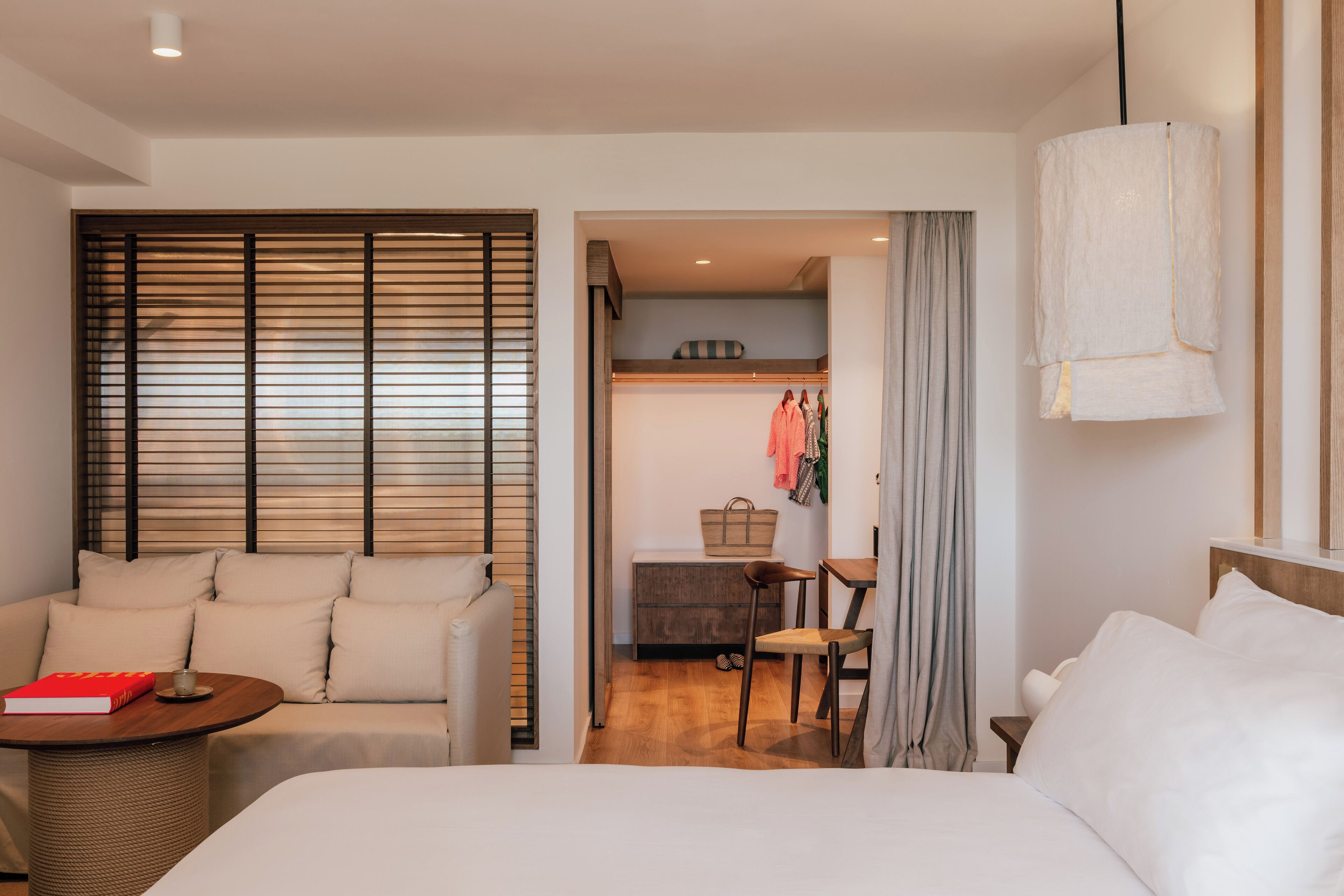 A hotel room with a bed, a sofa, a small table, and a chair. There is a kitchenette in the background.
