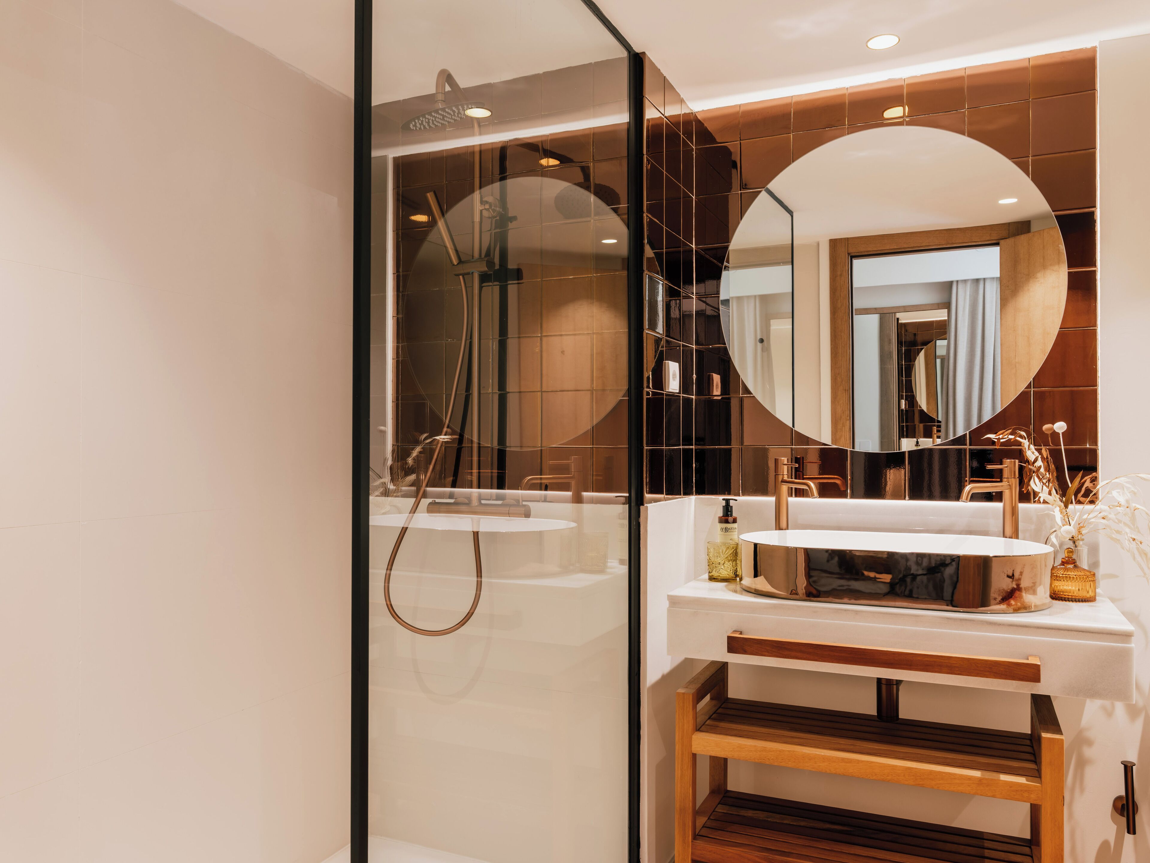 Une salle de bain moderne avec une douche à parois de verre, un miroir rond et un meuble-lavabo en bois.