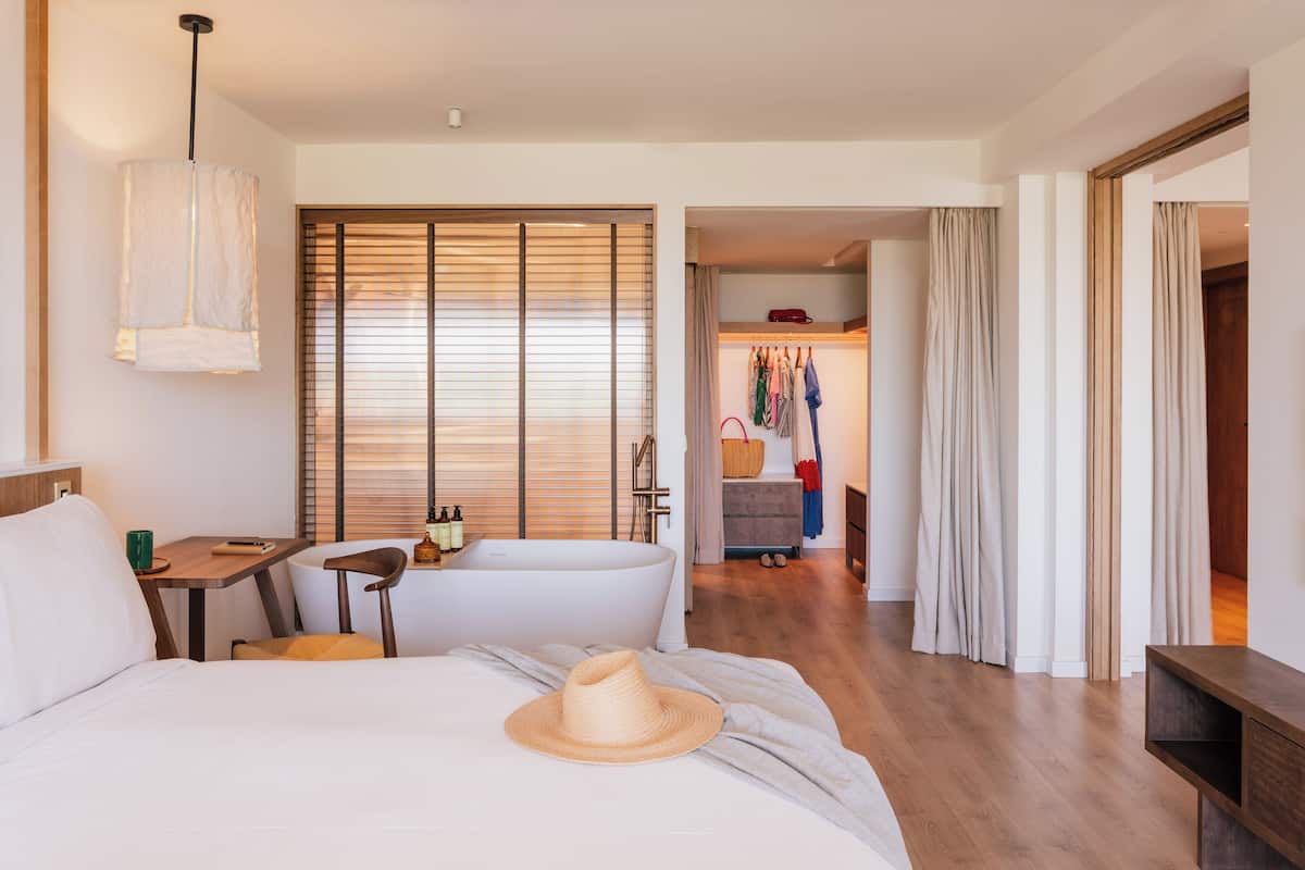 A hotel room with a bed, a desk, a chair, a wardrobe, and a bathroom visible through an open door.