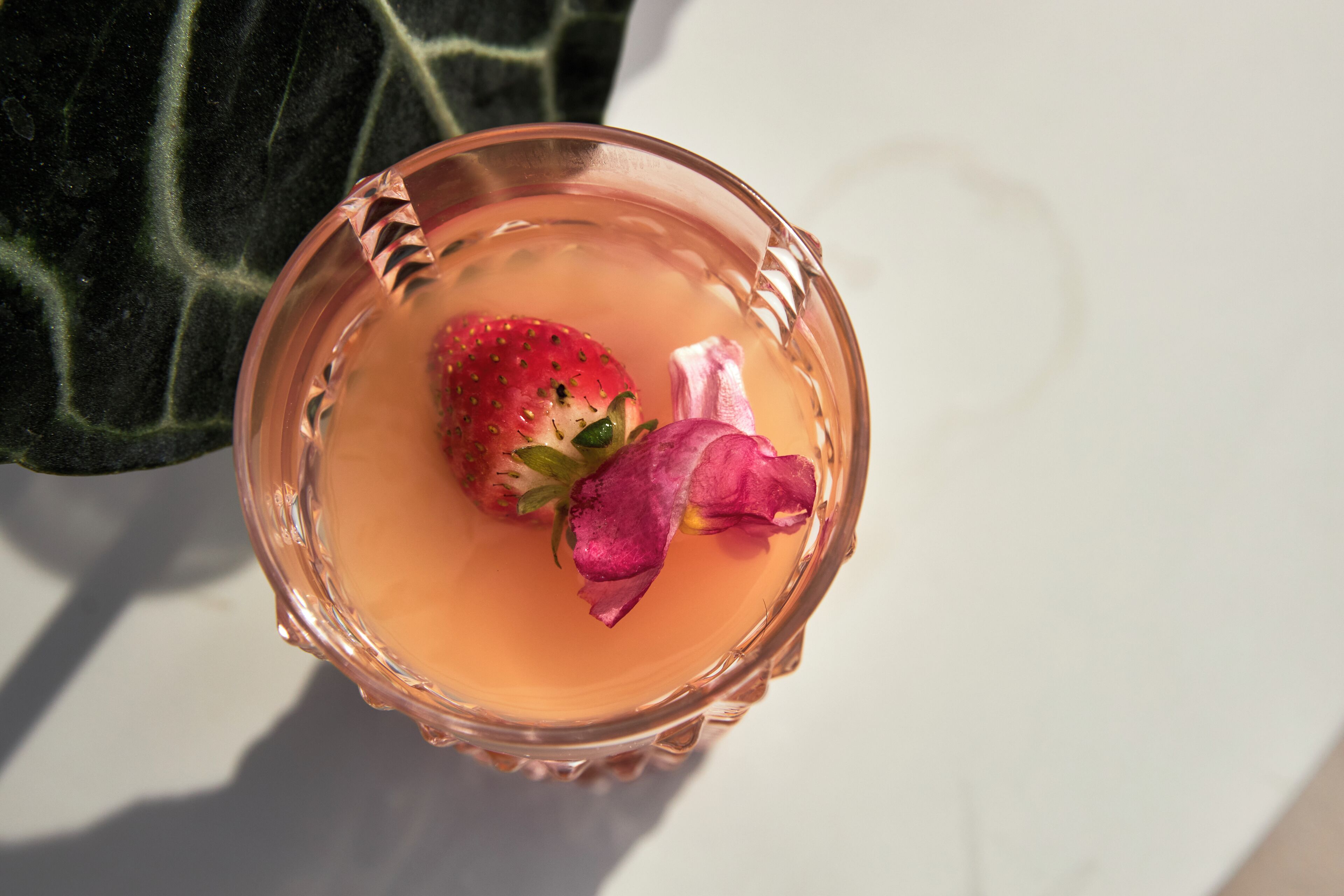 Ein Glas mit einem pinken Getränk, einer Erdbeere und einer Blume.