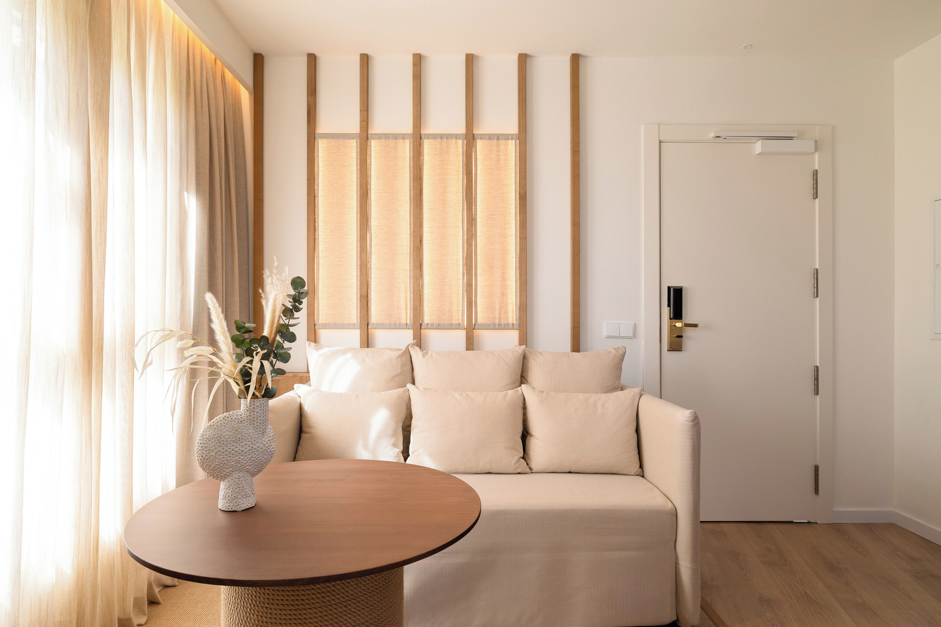 A modern living room with a beige sofa, a round wooden table, and a decorative vase.