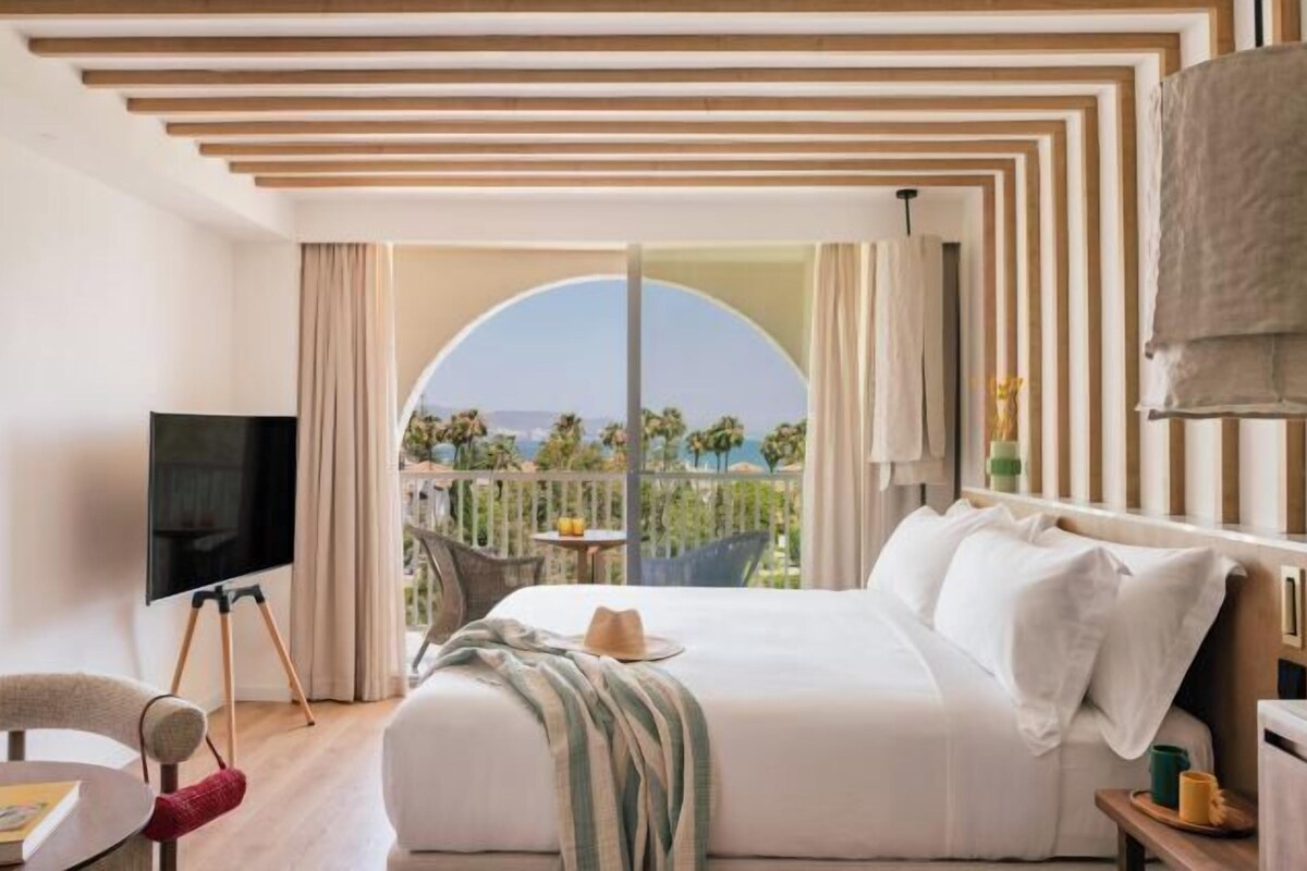 A hotel room with a bed, a TV, a balcony with a view, and a dining area.