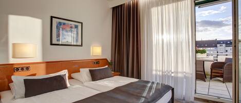 A hotel room with a large bed, a wooden headboard, two bedside lamps, a framed picture on the wall, and a view of the outside through a sliding glass door.