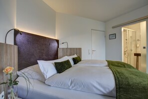 Um quarto moderno com uma cama grande, cabeceira de madeira, manta verde e um vaso com uma única flor.
