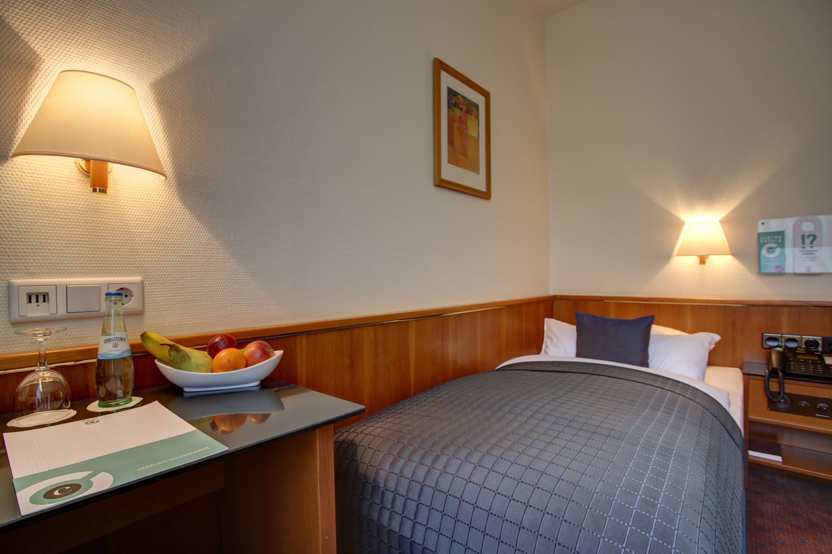 Habitación de hotel con cama, mesita de noche, lámpara y frutero.