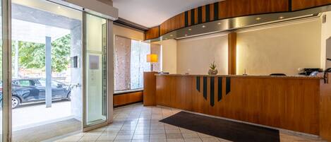 Una zona de recepción con un mostrador de madera, una puerta de vidrio y suelo de baldosas.