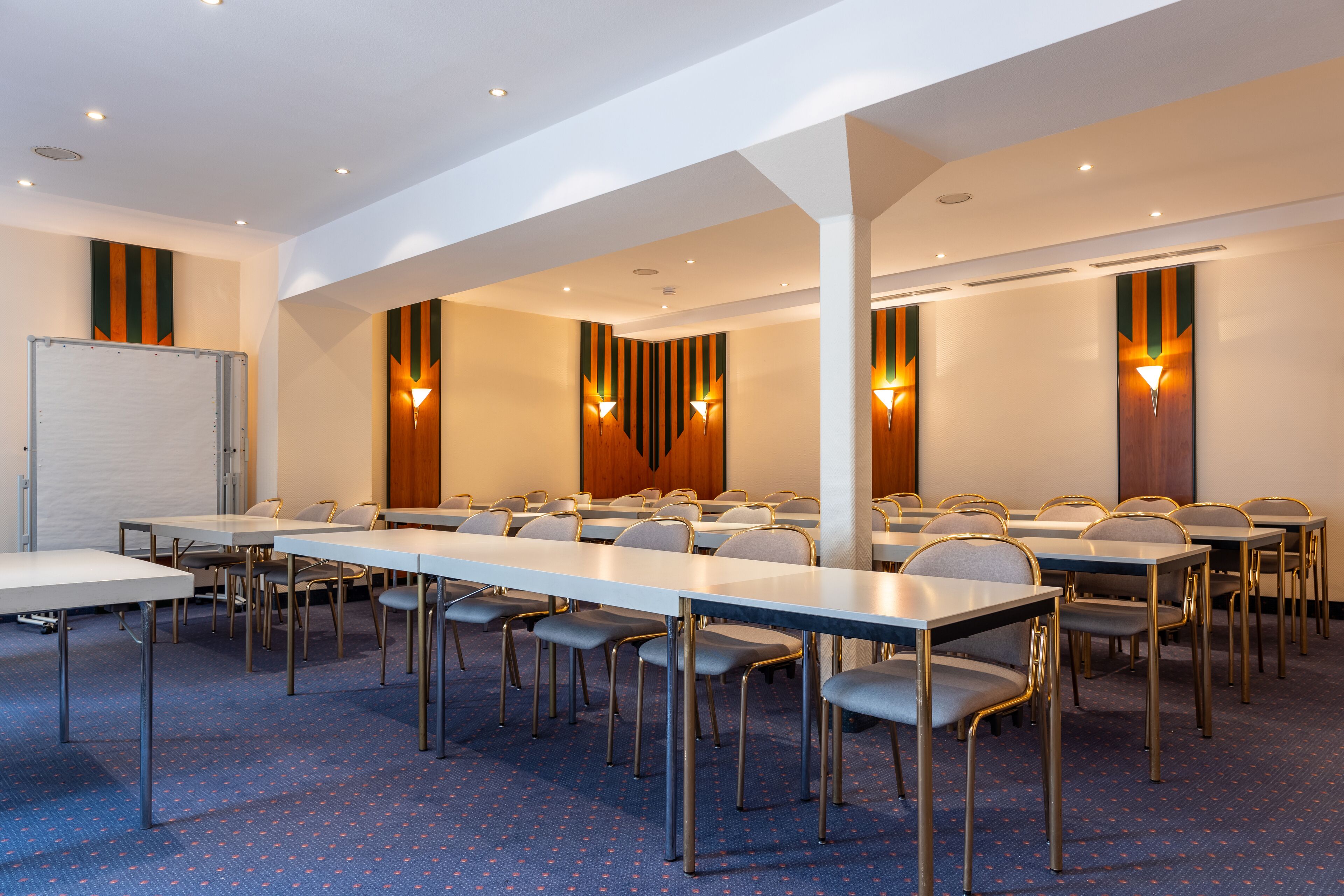 A conference room with multiple tables and chairs, equipped with overhead lighting and a whiteboard.